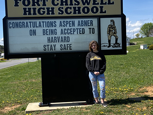 Aspen standing beside FCHS road sign saying congratulations on being accepted to Harvard