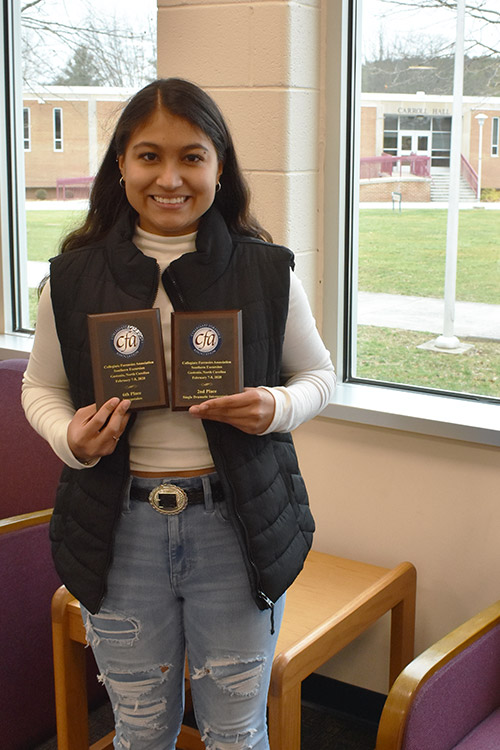 Natalia Garcia standing by windows on WCC campus, holding forensics award plaques